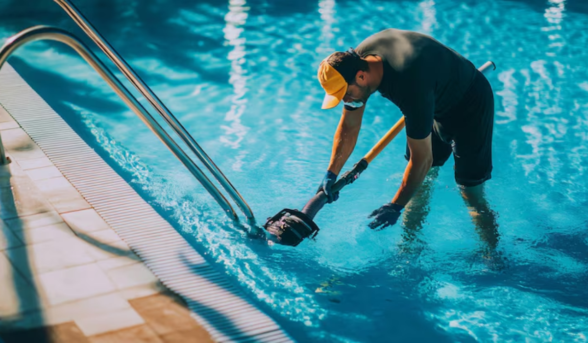 Professional pool cleaner using skimmer net to clean swimming pool surface, removing leaves and debris from crystal clear blue water